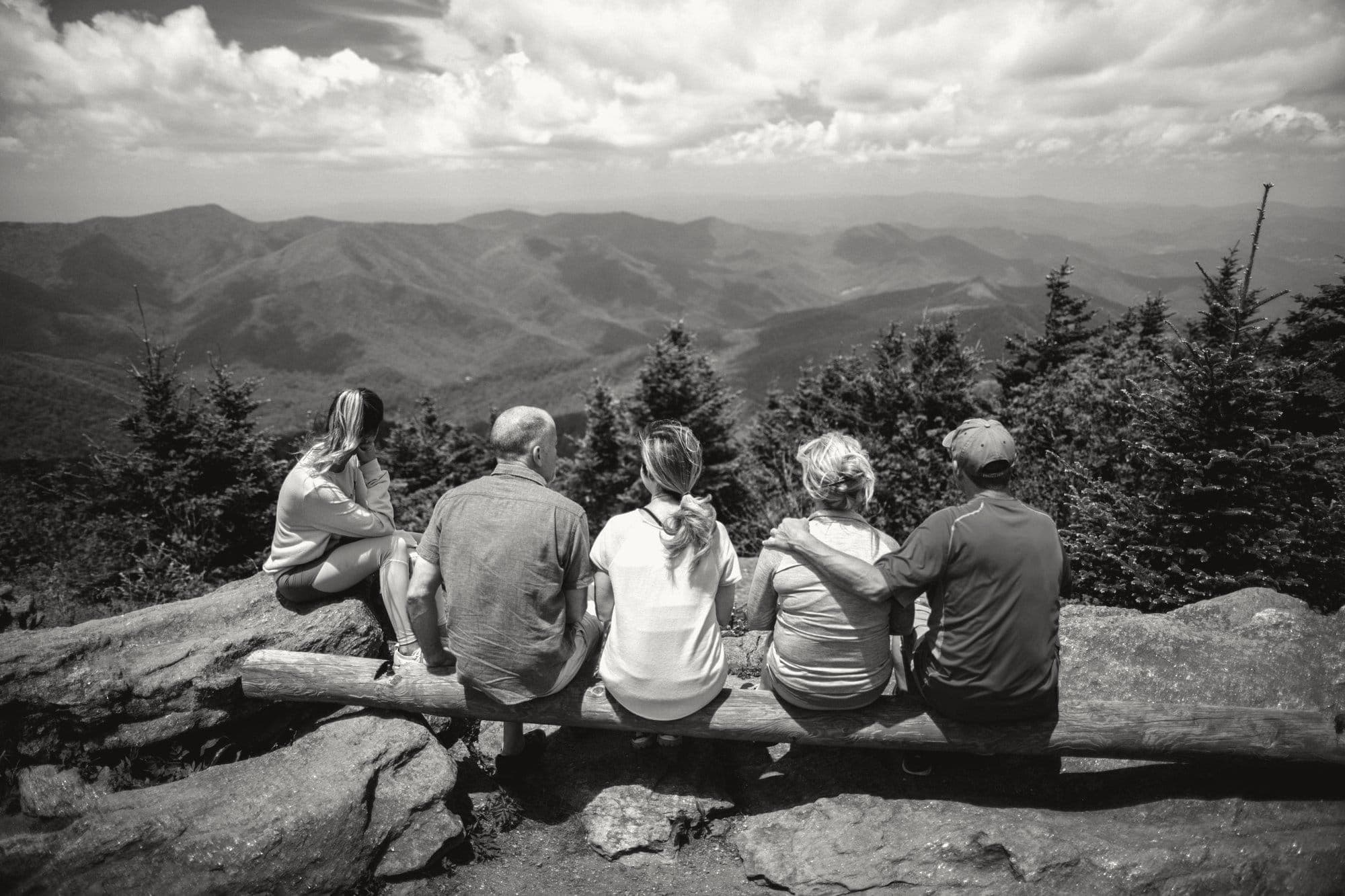 Five people sitting on a log at a mountain overlook